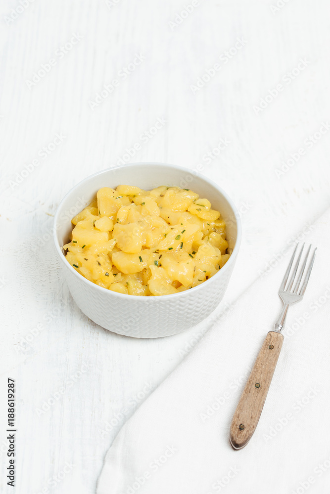 Bowl of traditional German , Austrian or Swiss potato salad made with oil, vinegar and chives, served in light grey bowl on white wooden background Bowl of traditional German , Austrian or Swiss potato salad made with oil, vinegar and chives, served in light grey bowl on white wooden background