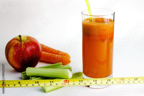 Dieting concept. Fresh, homemade, healthy carrot juice in a glass with carrots, celery, an apple and tape meausure on white background. Vegetable, slimming  juice. photo