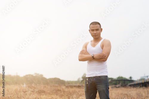 Asian young man in white vest and jeans standing on dry grass field