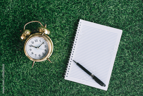 clock and blank notebook on a green grass. nature concept