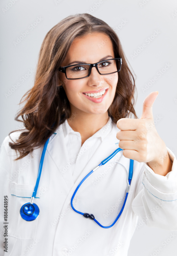 Female doctor with thumbs up gesture, over grey Female doctor with thumbs up gesture, over grey