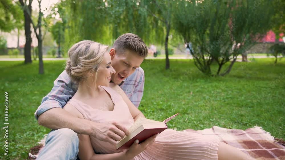 Guy reading book to his girlfriend, couple enjoying leisure in park together Guy reading book to his girlfriend, couple enjoying leisure in park together