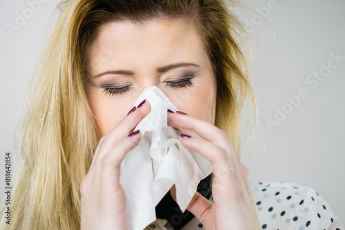 Woman being sick having flu sneeze into tissue