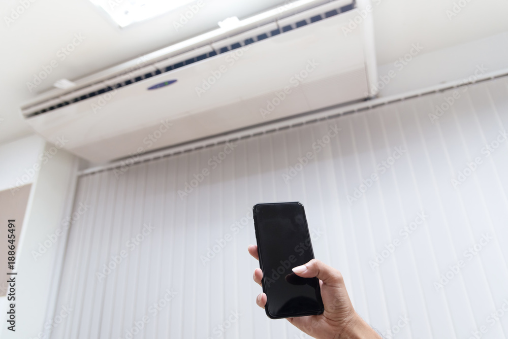 Hand holding smartphone as remote control setting air condition.. Hand holding smartphone as remote control setting air condition..