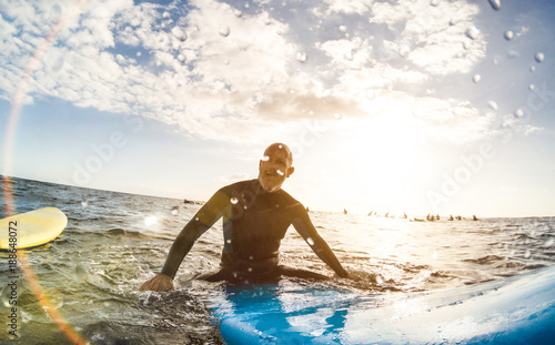 Fotografie Guy surfer relaxing on surfboard at sunset in Tenerife with unrecognizable peopl