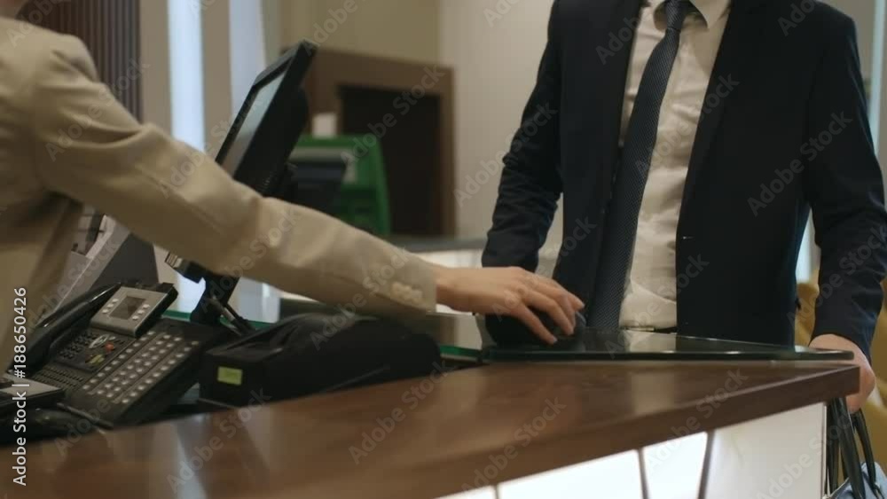 Unrecognizable female receptionist giving terminal to businessman paying with credit card at check-in desk in hotel Unrecognizable female receptionist giving terminal to businessman paying with credit card at check-in desk in hotel