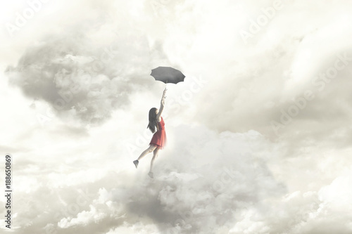 Surreal moment of an elegant woman flying in the middle of the clouds hanging on her umbrella