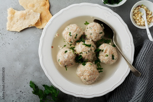 Homemade chicken matzo ball soup with parsley and garlic in simple white ceramic plate on a gray stone or concrete background.  Traditional Jewish passover dish. Selective focus. Top view.
