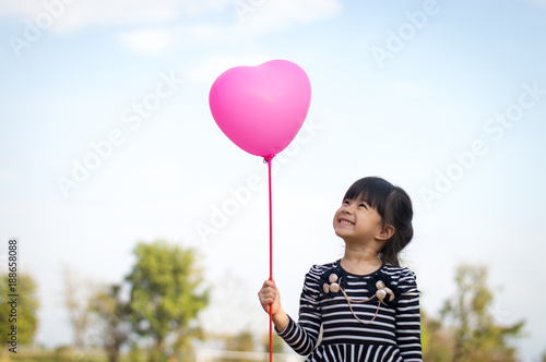 Happy little asian girl holding pink balloon in hand selective focus.