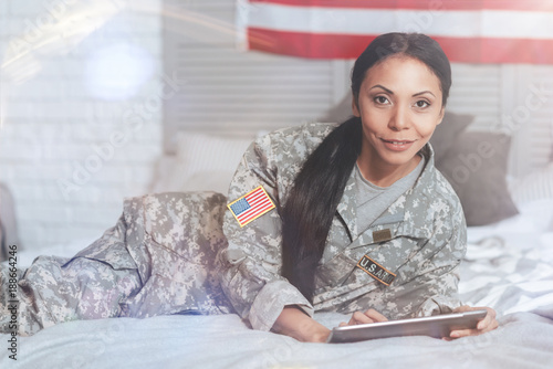 Military officer. Pleasant nice attractive woman holding a tablet and looking at you while working as a military officer
