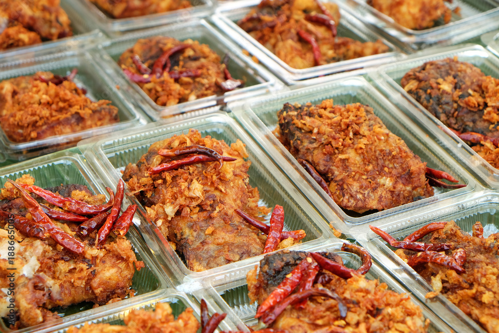 Many pieces of deep fried fish with the garlic and red chili in plastic boxes
