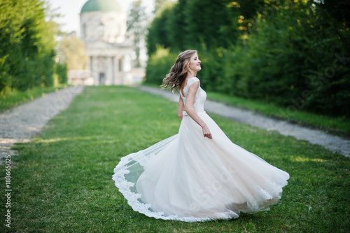 Lonely attractive bride walking on the green alley which leads to a church.