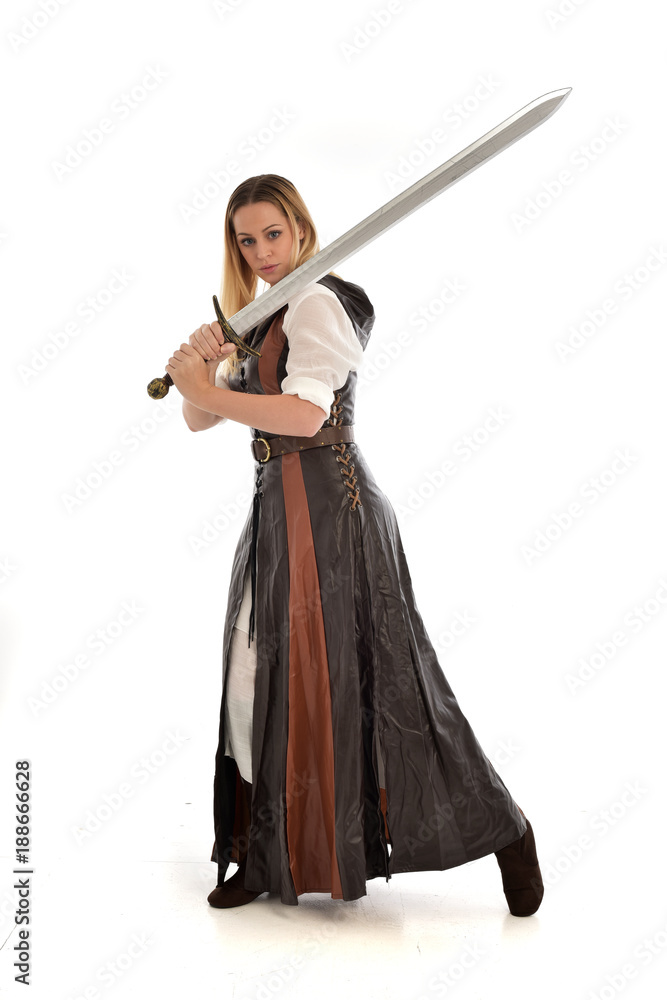 full length portrait of girl wearing brown fantasy costume, holding a sword. standing pose on white studio background. full length portrait of girl wearing brown fantasy costume, holding a sword. standing pose on white studio background.