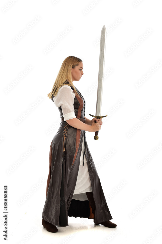 full length portrait of girl wearing brown fantasy costume, holding a sword. standing pose on white studio background. full length portrait of girl wearing brown fantasy costume, holding a sword. standing pose on white studio background.
