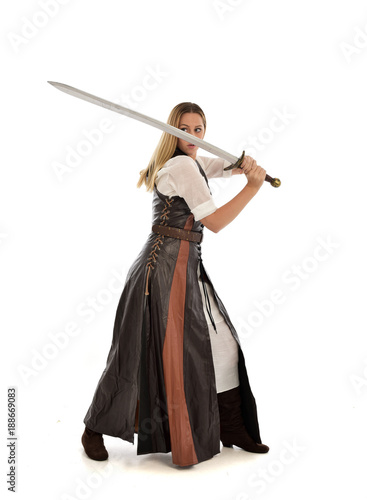 full length portrait of girl wearing brown fantasy costume, holding a sword. standing pose on white studio background. 