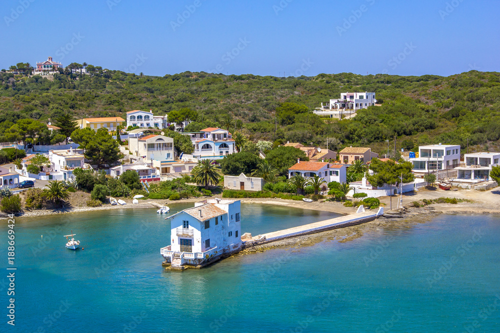 View from the sea to a small town in Balearis Minor, moored boats, boats and yachts, and a small house on the pier in the bay, Spain