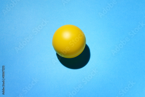 Pallina di gomma di color giallo su fondo blu e ombra di appoggio