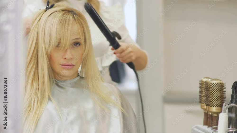 Hairdresser makes stylish hairstyle with curling iron Hairdresser makes stylish hairstyle with curling iron
