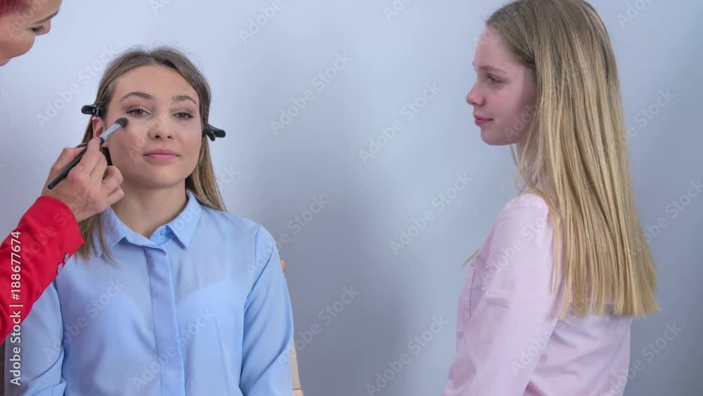 A make up artist applies make up on the client's face. Another girls stands there and she asks questions about the make up session. A make up artist applies make up on the client's face. Another girls stands there and she asks questions about the make up session.