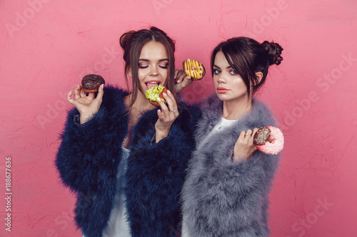 Beautiful girls with donuts posing on pink background.