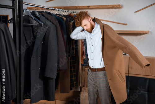 handsome young man wearing stylish brown overcoat in boutique