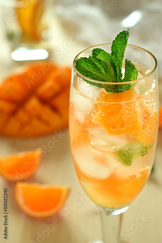 Sparkling cocktail with mango pieces, ice cubes and mint in a wineglass