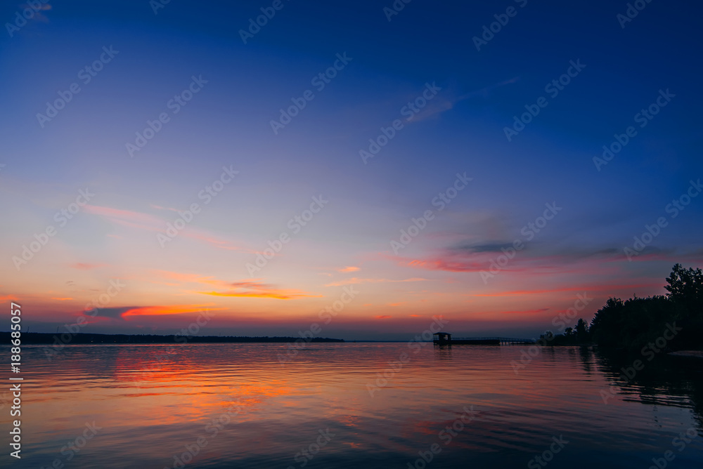 sunset over water of river with a pier and a beach with beautiful red and blue sky