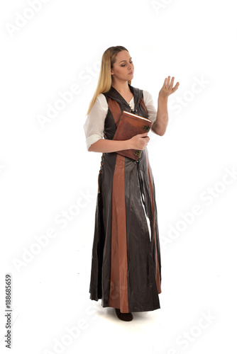  full length portrait of girl wearing brown fantasy costume, holding a book. standing pose on white studio background. 