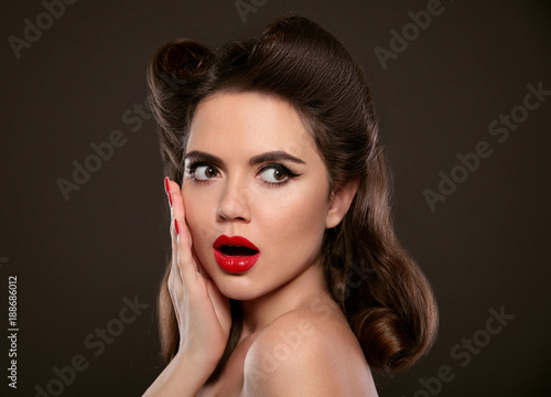 Surprised pin up girl holds cheek by hand. Comic woman with curls retro hair style. Wow. Presenting your product. Shocked lady isolated on black dark studio background.