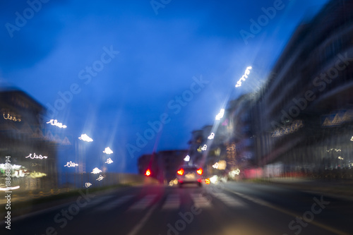 a walkway and a car on a night street, lit by the shrubs and blurred shadows. traces of cars and street lighting in a big night city.
