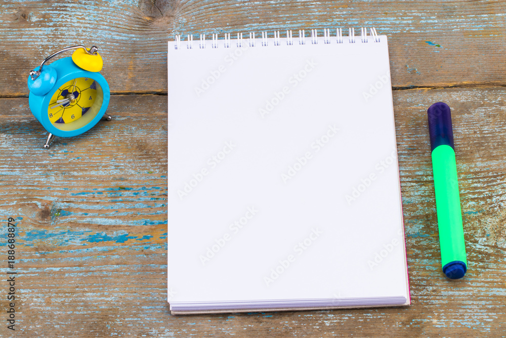 Fotografie Notebook and alarm clock on wooden background. With copy space