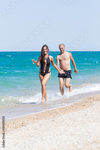 Barefoot young woman and man swimwear running along seashore