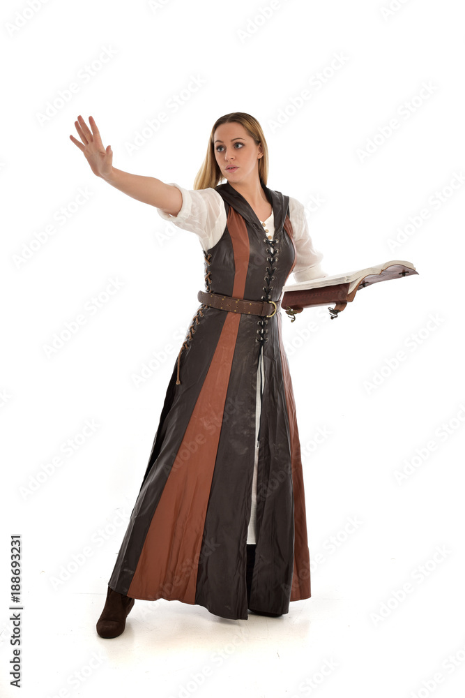  full length portrait of girl wearing brown  fantasy costume, holding a book. standing pose on white studio background. 