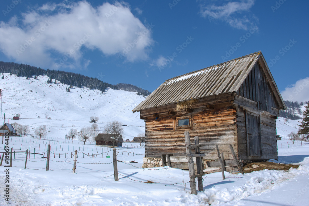 Wooden barn in the winter/Winter image with an old village wooden barn in the foreground and snowy hills in the background.