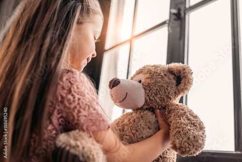 Fotografia adorable little child playing with teddy bear on windowsill
