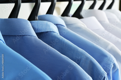 Clean shirts hanging on rack in laundry, closeup