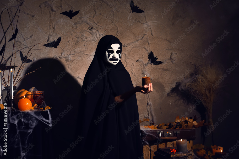 Mystic creature in black cloak holding candle in darkness Mystic creature in black cloak holding candle in darkness