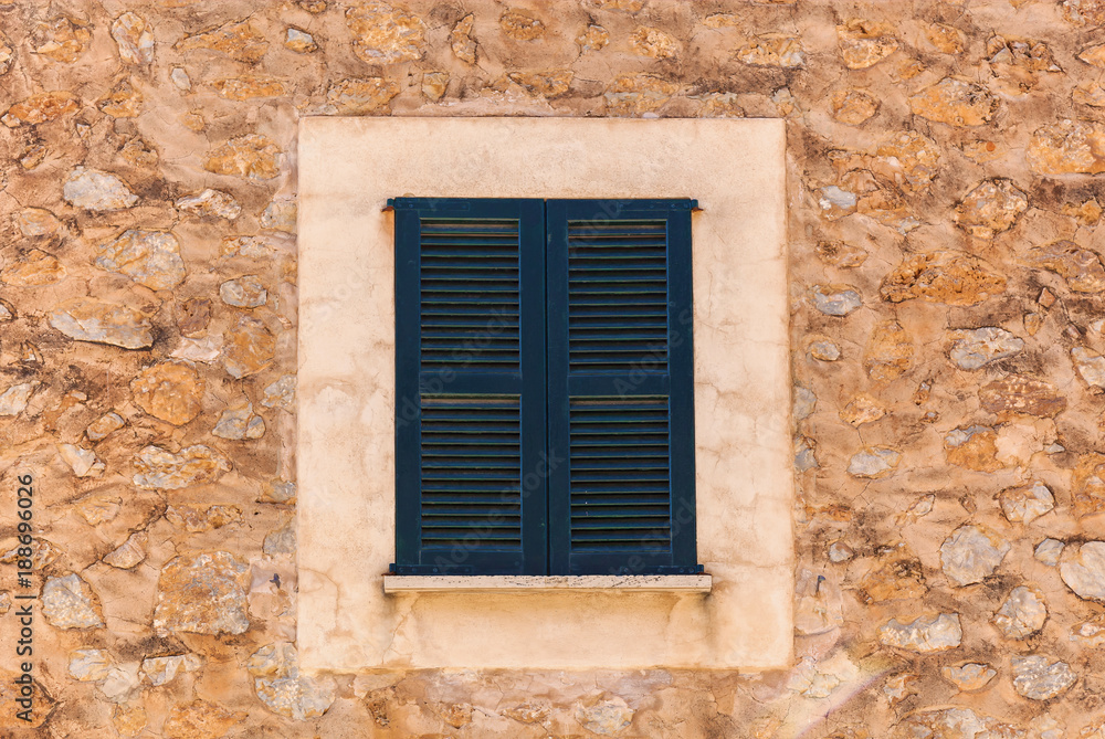 Old rustic stone house wall with closed window shutters, detail close-up, mediterranean background texture.wooden shutters Old rustic stone house wall with closed window shutters, detail close-up, mediterranean background texture.wooden shutters