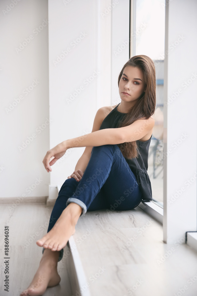 Depressed young woman after breakup sitting on window sill indoors Depressed young woman after breakup sitting on window sill indoors