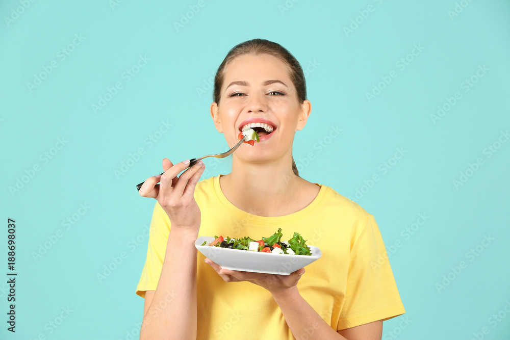 Young beautiful woman eating fresh salad on color background Young beautiful woman eating fresh salad on color background