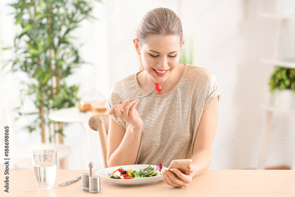 Young beautiful woman with phone eating fresh salad at home