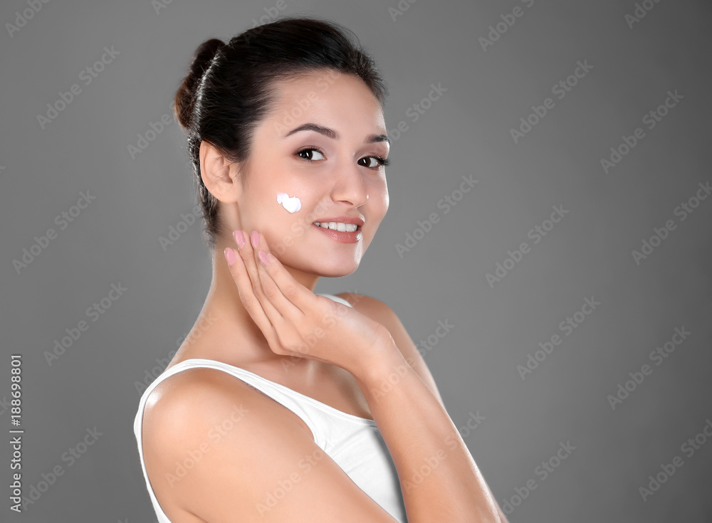 Attractive young woman applying face cream on grey background Attractive young woman applying face cream on grey background