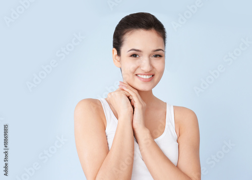 Attractive young woman with silky skin after applying cream on color background