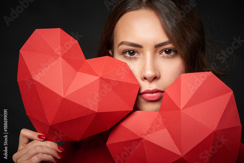 Closeup of woman in red holding two red heart shapes over dark background photo