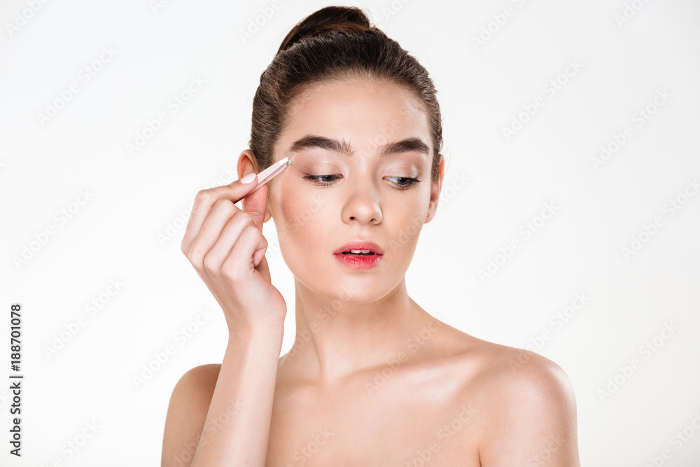 Close up photo of young cute woman with soft skin plucking eyebrows with tweezers isolated over white background