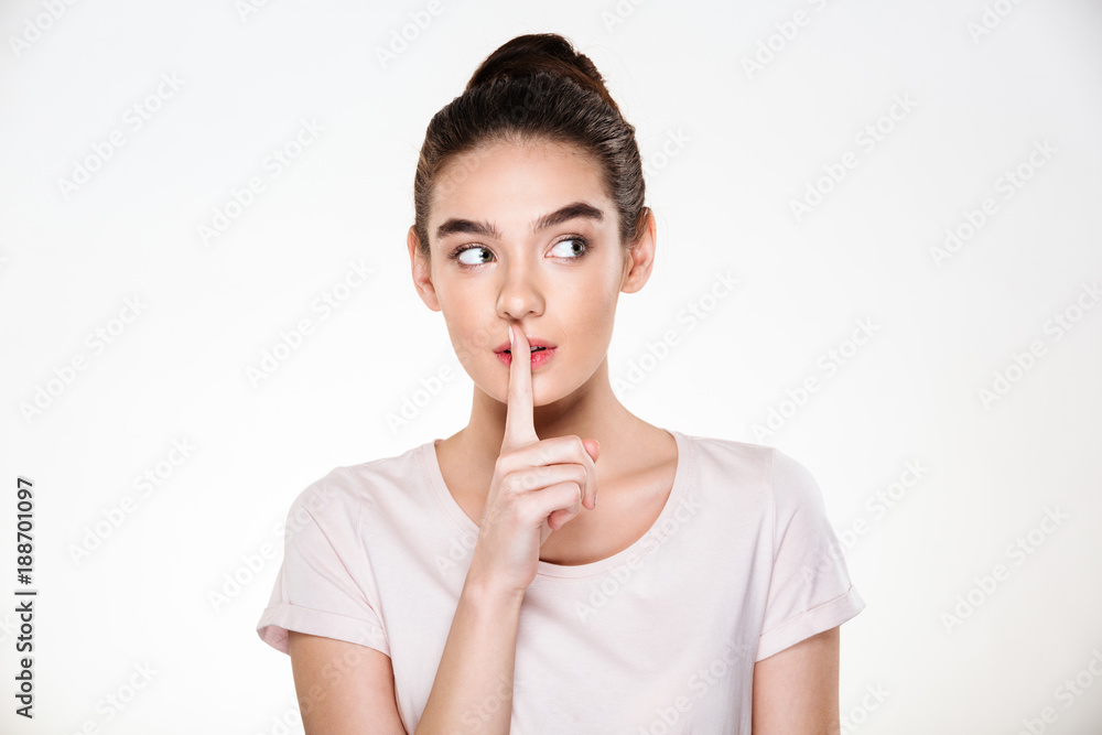Portrait of beautiful pensive young woman with perfect skin holding index finger on lips asking to keep silence or secret over white background Portrait of beautiful pensive young woman with perfect skin holding index finger on lips asking to keep silence or secret over white background