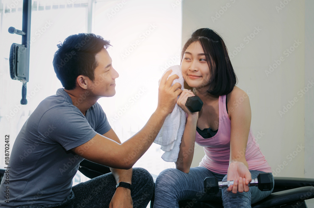 muscular young handsome man helping wipes sweat off young asian woman face while resting after workout in fitness gym, love couple, personal trainer, bodybuilder, lifestyle and sport exercise concept muscular young handsome man helping wipes sweat off young asian woman face while resting after workout in fitness gym, love couple, personal trainer, bodybuilder, lifestyle and sport exercise concept