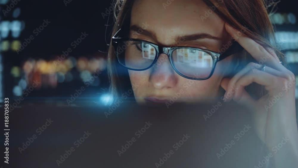 Portrait of attractive young businesswoman working on modern computer or laptop at new office with a view of the night city, Skyscrapers on the background, beautiful female employer using computer