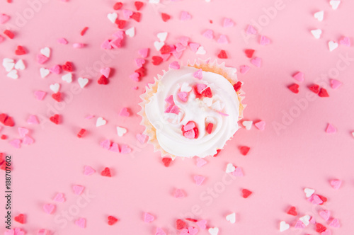 cup cake with white icing and heart sprinkles on a pink background for valentine's day