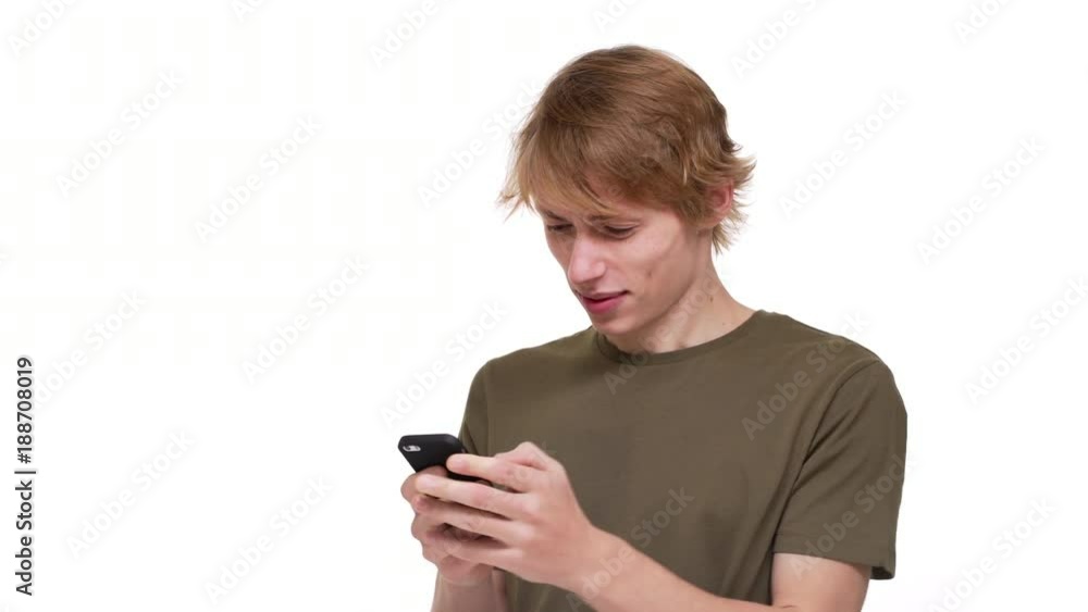 Portrait of involved man in green t-shirt using cell phone playing online games or chatting over white background. Concept of emotions Portrait of involved man in green t-shirt using cell phone playing online games or chatting over white background. Concept of emotions